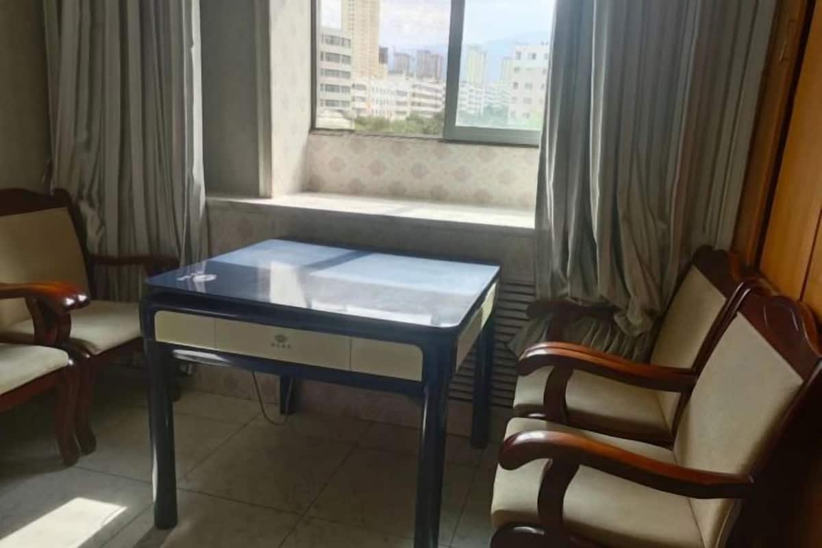 Ein Zimmer mit einem Tisch, zwei Stühlen, einem Fenster mit Vorhängen und Blick auf Gebäude.