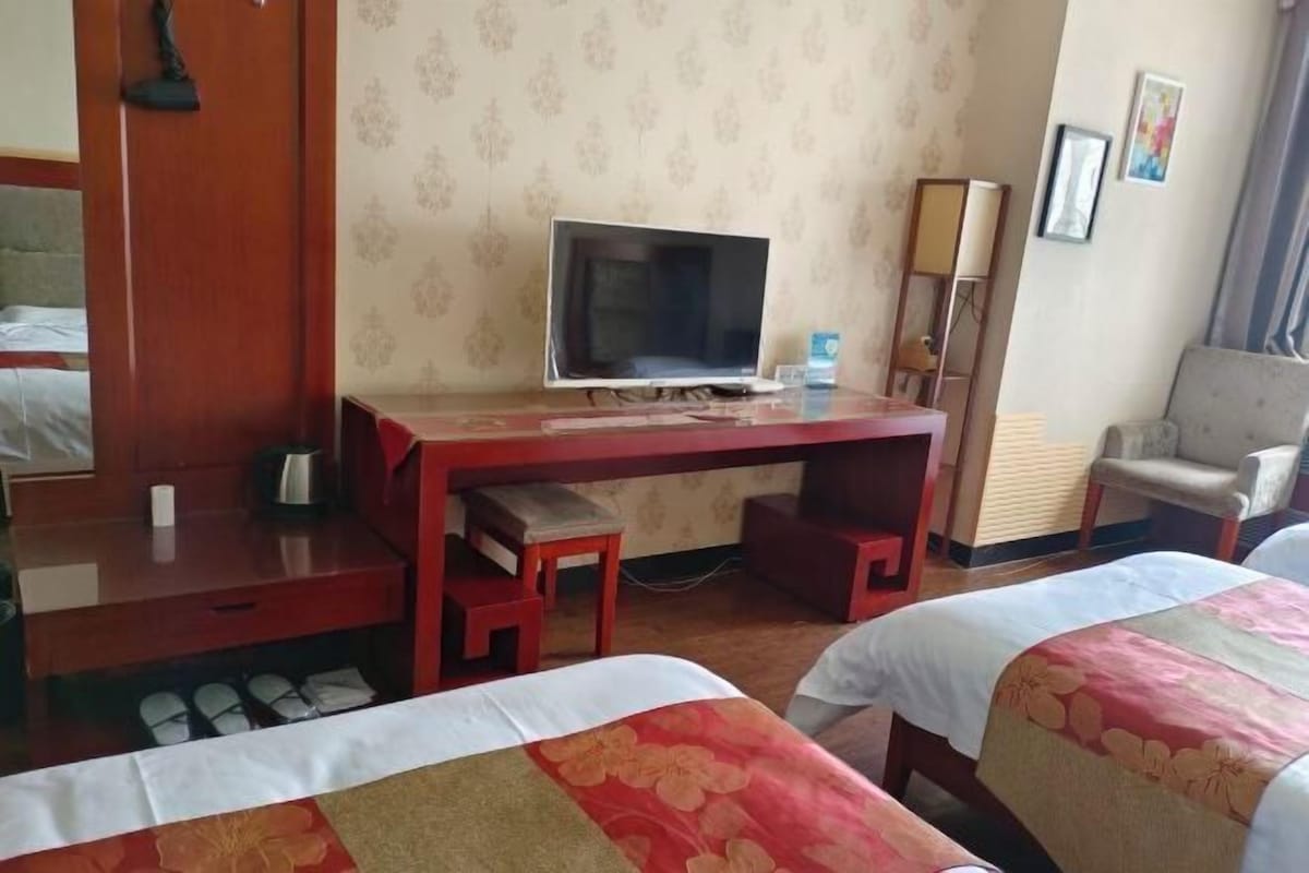 Hotellihuone, jossa on puinen työpöytä, televisio, kaksi sänkyä, joissa on kukalliset päiväpeitteet, tuoli ja vaatekaappi.