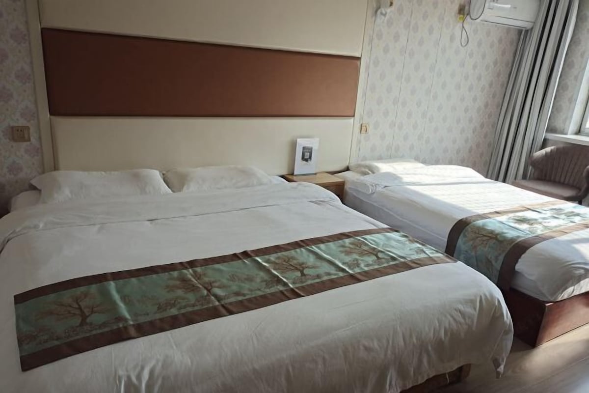 Hotellihuone, jossa on kaksi sänkyä, sängynpääty, yöpöytä ja tuoli.