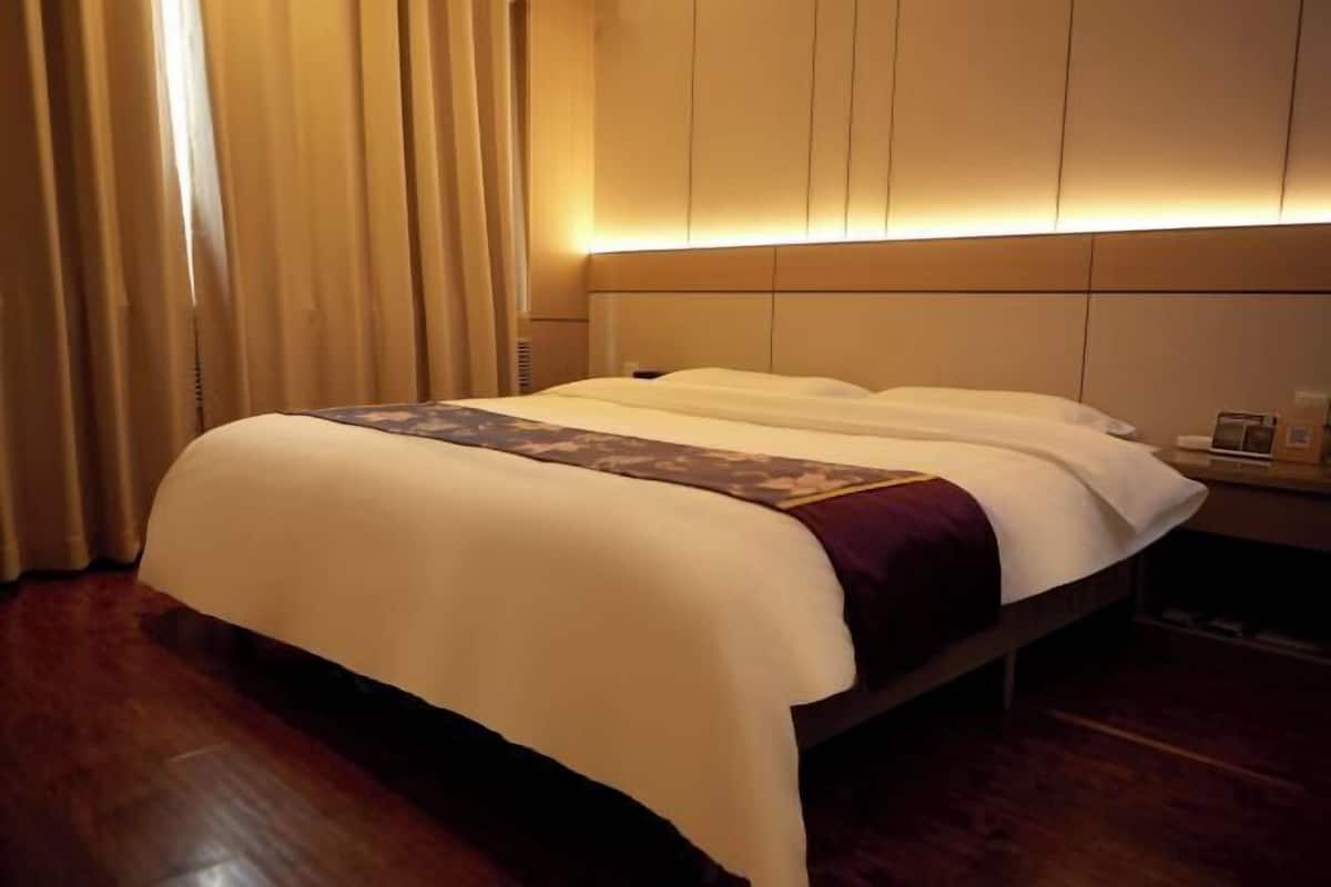 Ein Hotelzimmer mit Bett, Vorhängen, Nachttisch und einer Wandleuchte.