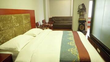 A hotel room with a bed, a sofa, and a clock on a stand.