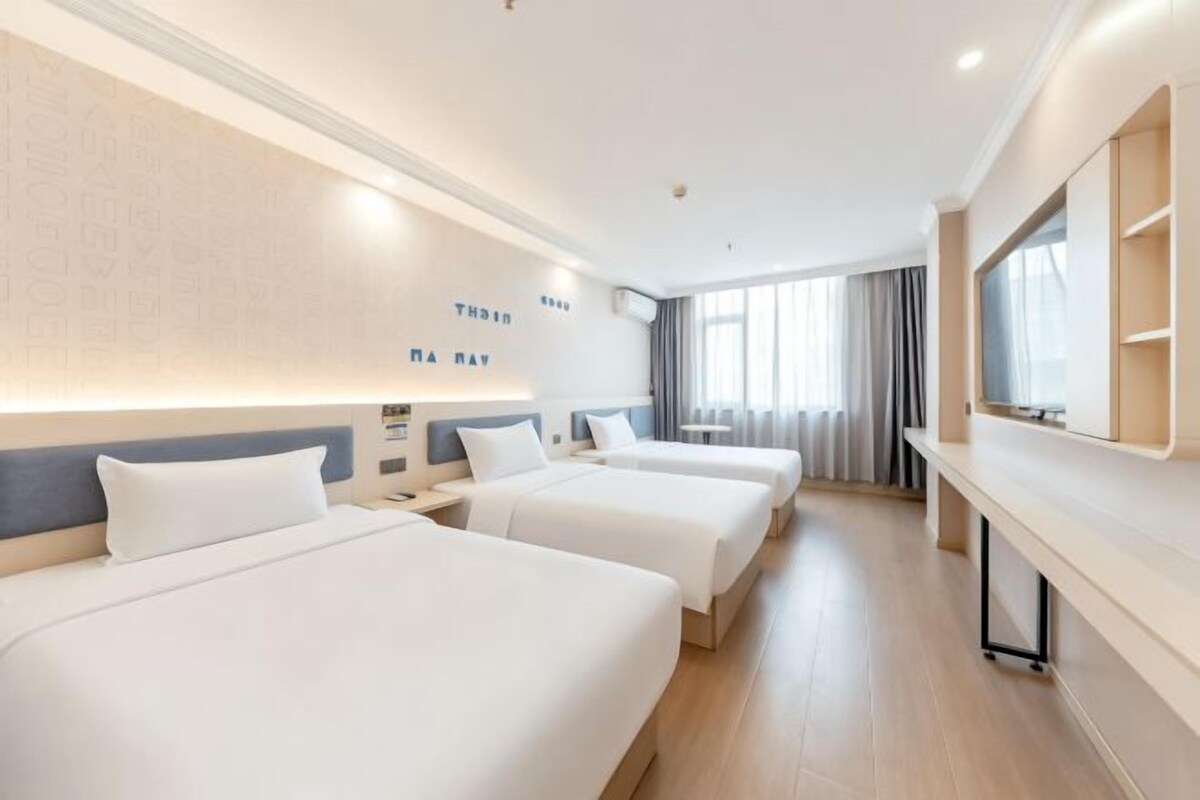 A hotel room with three beds, a large mirror, and a window with curtains.