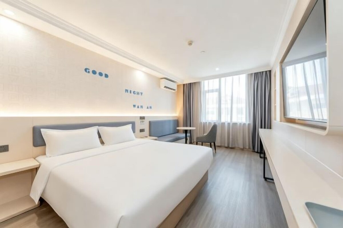 A hotel room with a large bed, a desk, and a window with curtains.