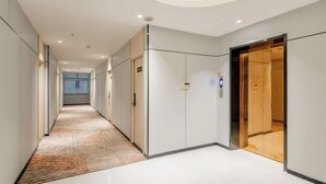 Un couloir d’hôtel avec un sol recouvert de moquette, un ascenseur en bois et une porte en verre.