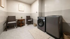 Une buanderie équipée d’un lave-linge, de deux fauteuils en osier, d’une petite table avec une plante et d’un sol carrelé.