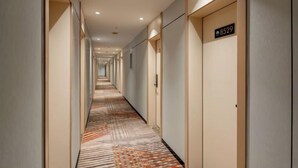 Un couloir d’hôtel avec des portes portant les numéros des chambres, une moquette à motifs et un design moderne.