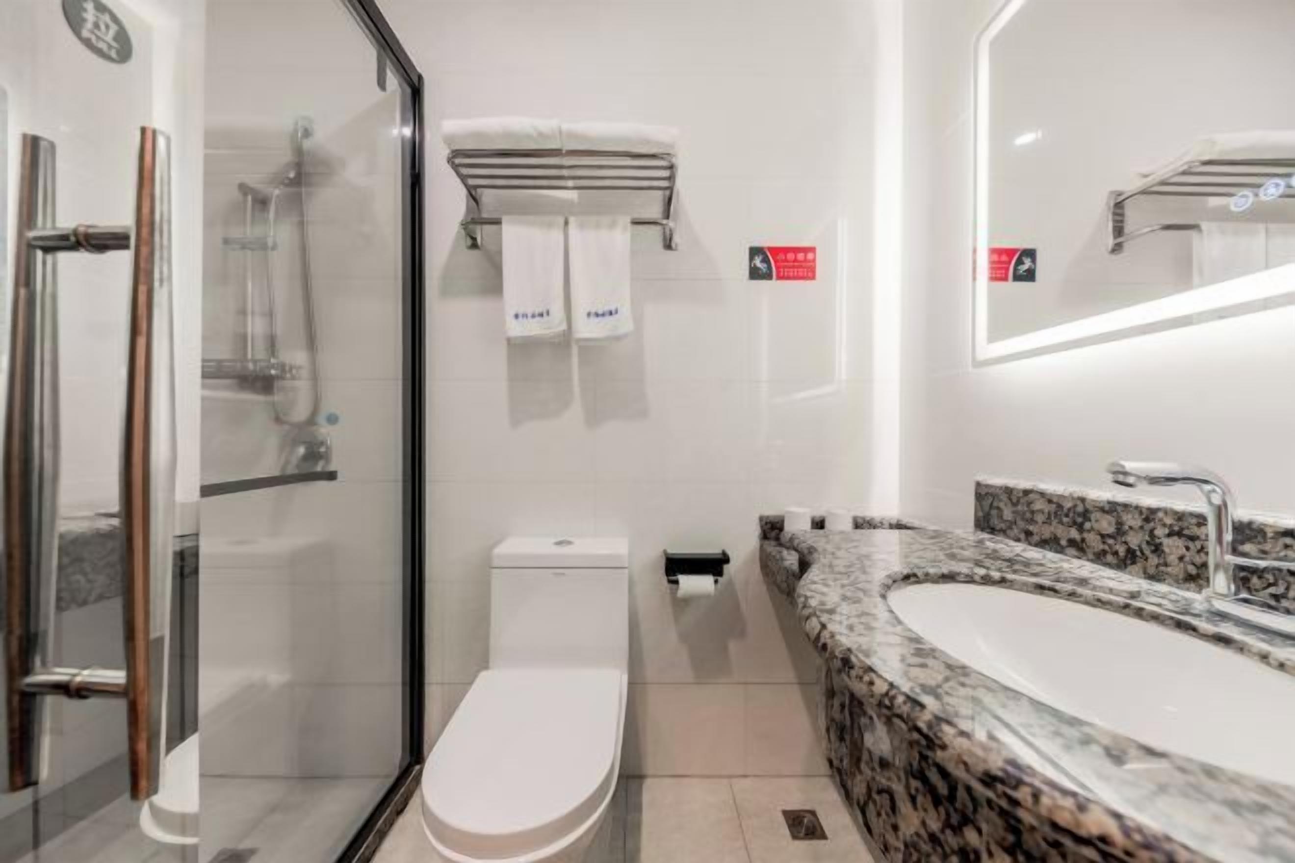 A modern bathroom with a glass shower enclosure, a toilet, a sink with a granite countertop, and a mirror with integrated lighting.