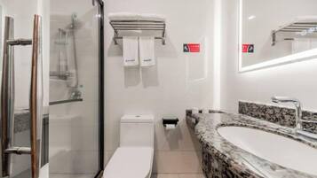 A modern bathroom with a glass shower enclosure, a toilet, a sink with a granite countertop, and a mirror with integrated lighting.