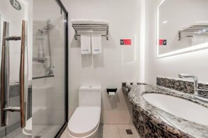 Un baño moderno con cabina de ducha de vidrio, inodoro, lavabo con encimera de granito e iluminación integrada en el espejo.