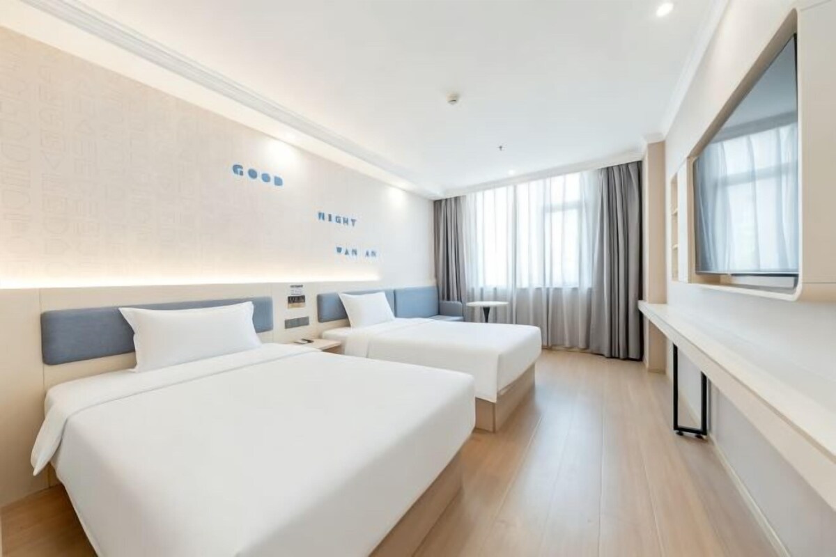 A hotel room with two beds, a TV, and a large window.