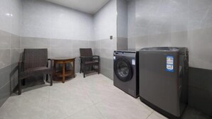 A compact laundry room with a washing machine and dryer, two wicker chairs, and a small wooden table. - Ribera Cloud Hotel (Shanghai Jinshan Petrochemical Branch) (Shanghai)