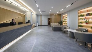 A modern reception area with a marble reception desk, seating area with sofas and a coffee table, and a wall with shelves displaying potted plants. - Ribera Cloud Hotel (Shanghai Jinshan Petrochemical Branch) (Shanghai)