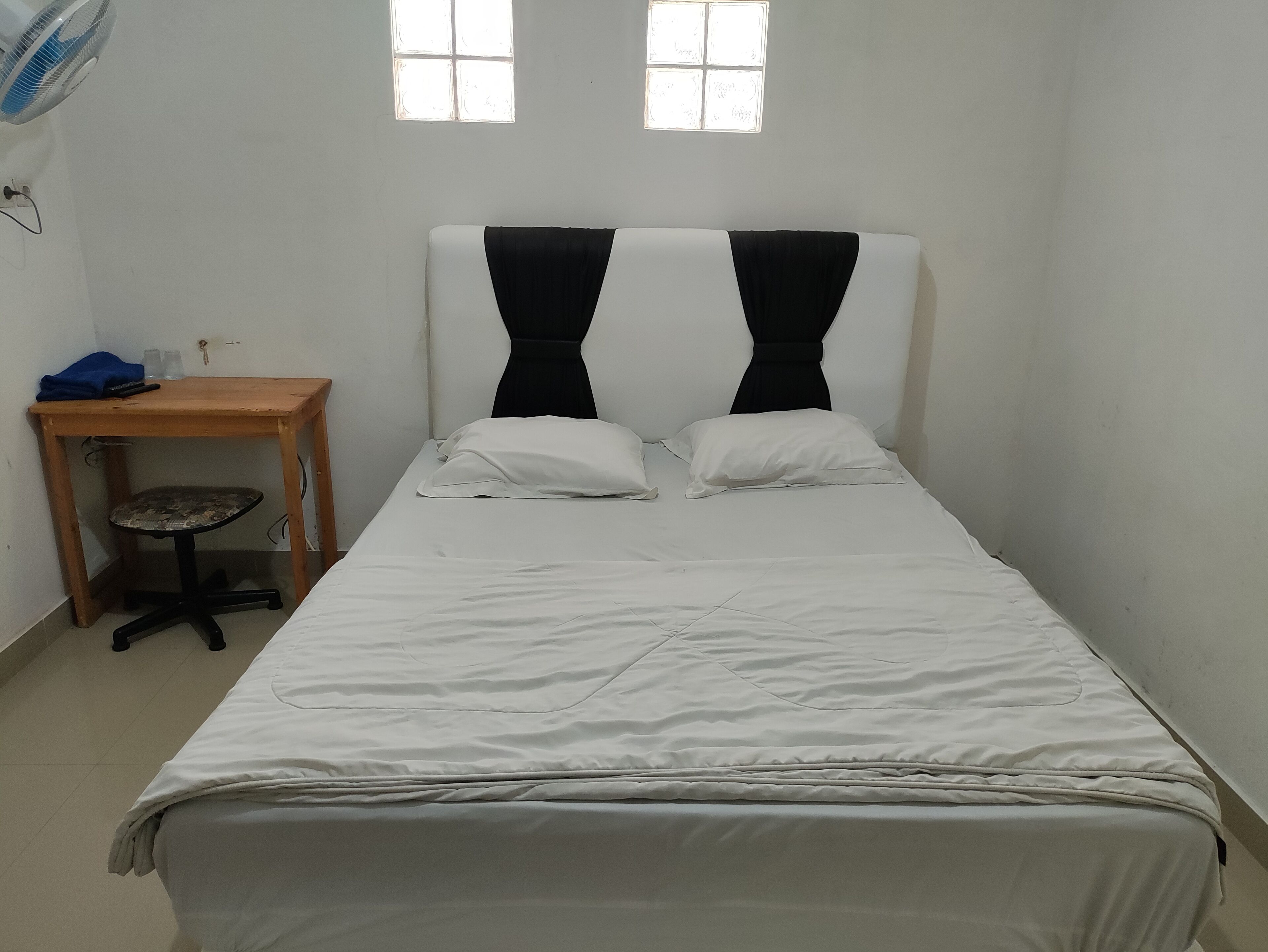 Una stanza piccola e pulita con un letto, una scrivania e due finestre.