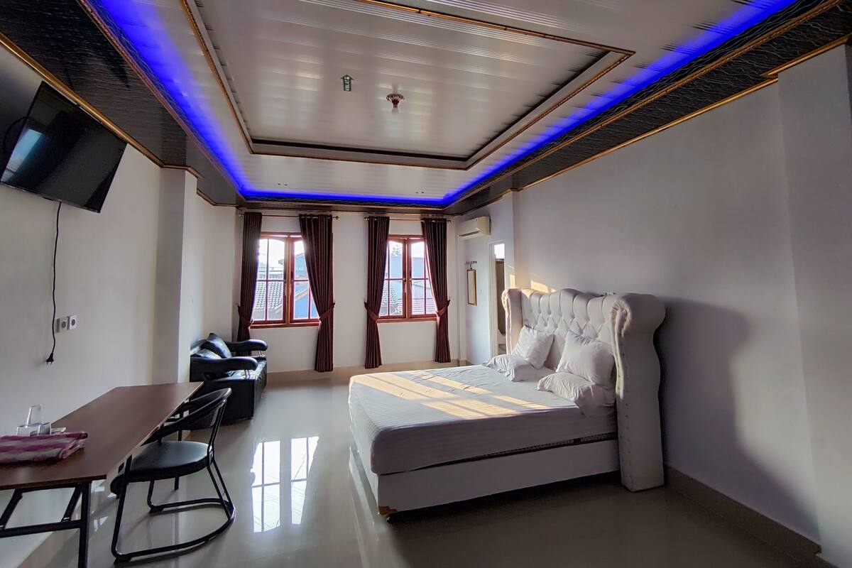 Een moderne slaapkamer met een groot bed, een bureau en een aan de muur bevestigde televisie.