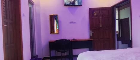 Un dormitorio con cama, escritorio, silla y televisión en la pared.