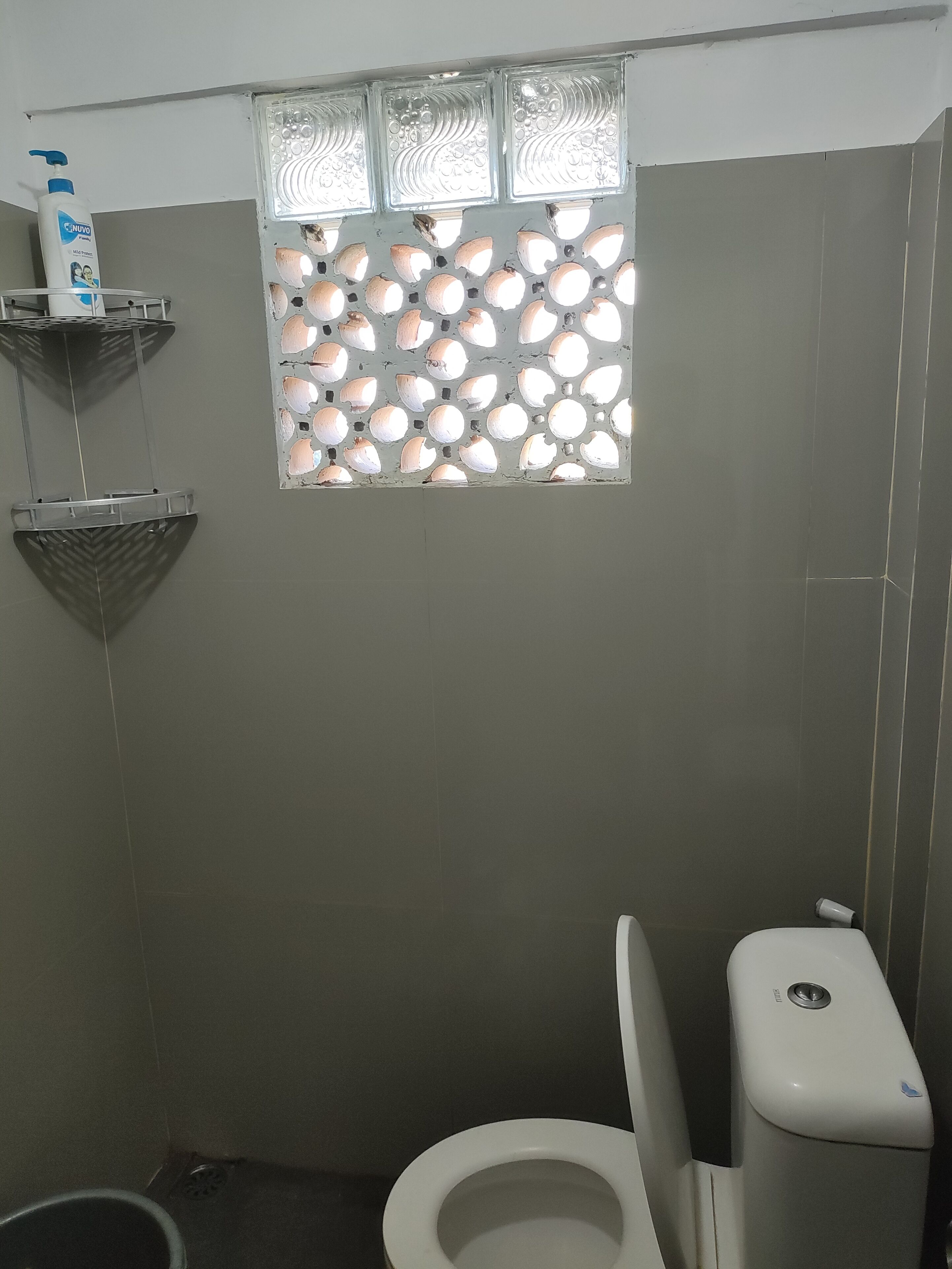 A bathroom with a toilet, a window with a decorative pattern, and a hand sanitizer dispenser on a shelf.