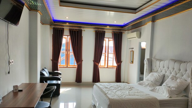 Une chambre d’hôtel avec un lit, un bureau, une chaise et deux fenêtres équipées de rideaux.