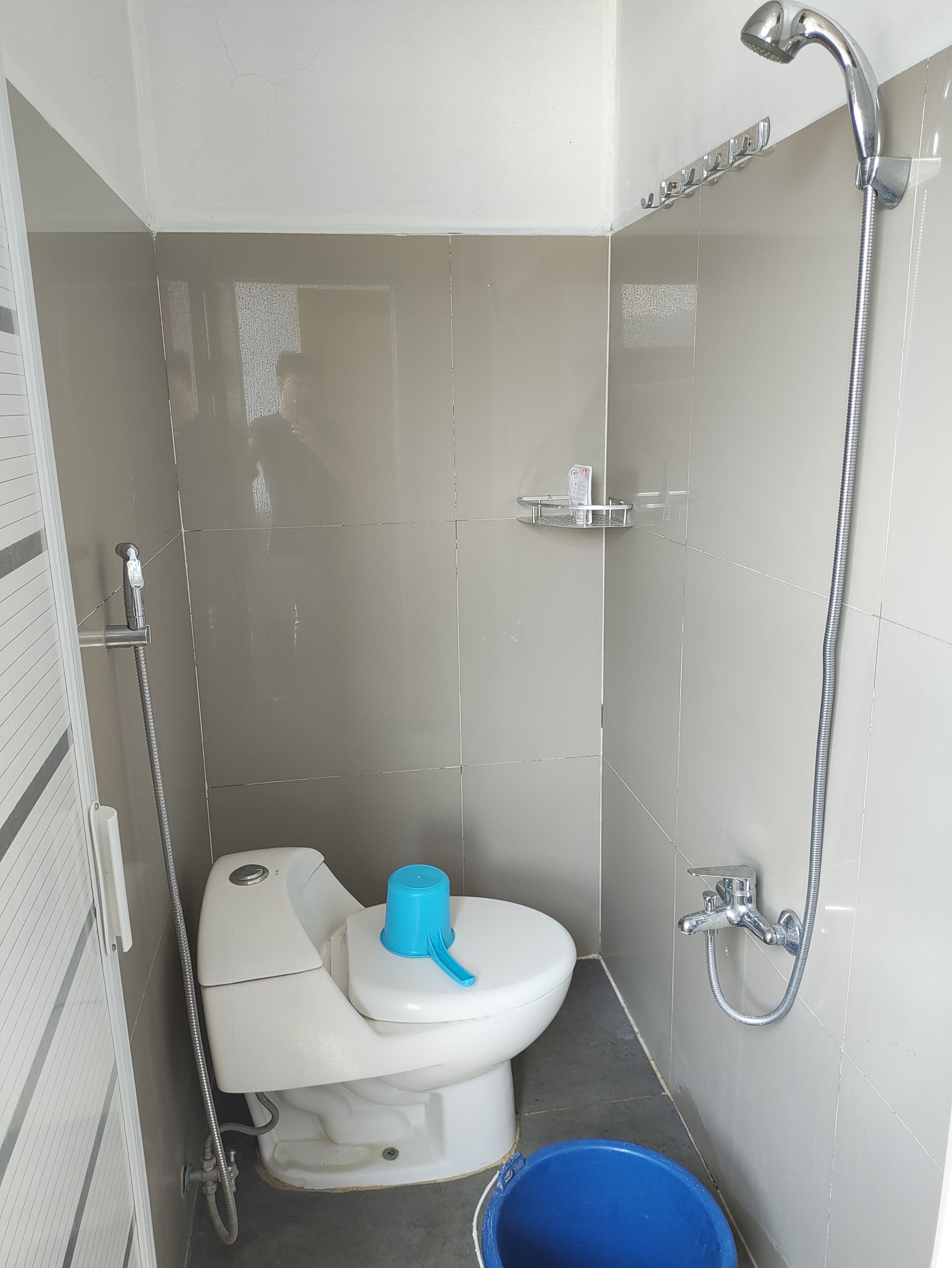 A small bathroom with a toilet, a shower, and a blue bucket.