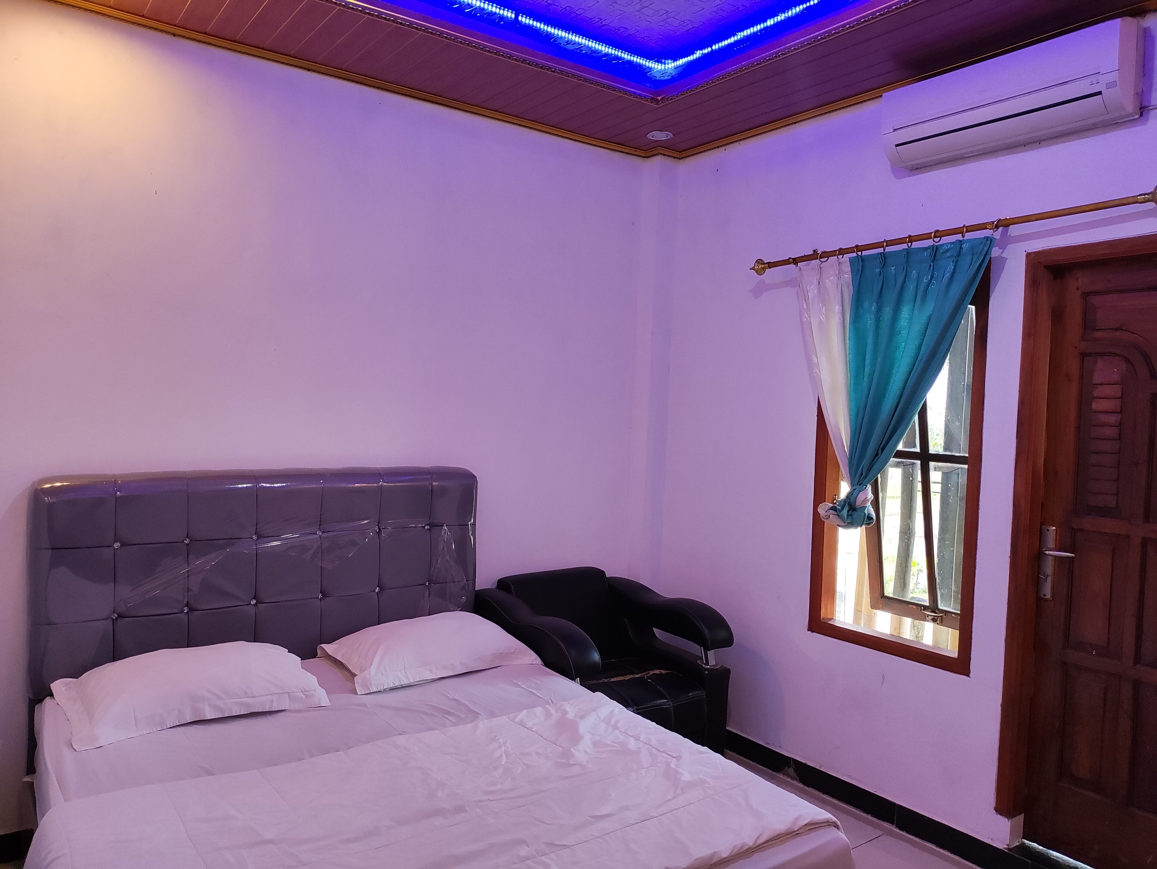 Een slaapkamer met een bed, een hoofdbord, een raam met gordijnen, een airconditioning en een houten deur.