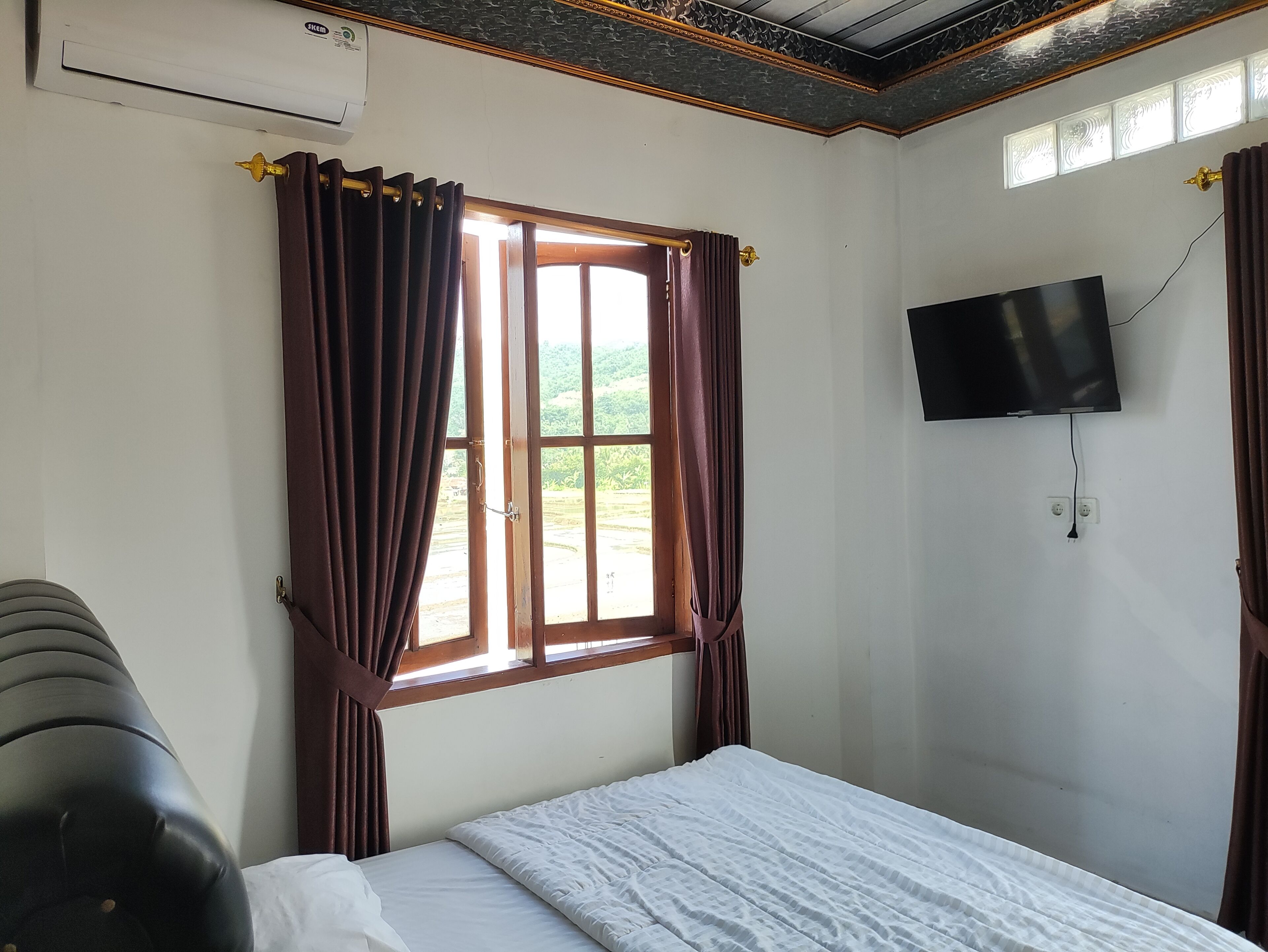 A room with a bed, a TV mounted on the wall, and a window with curtains.