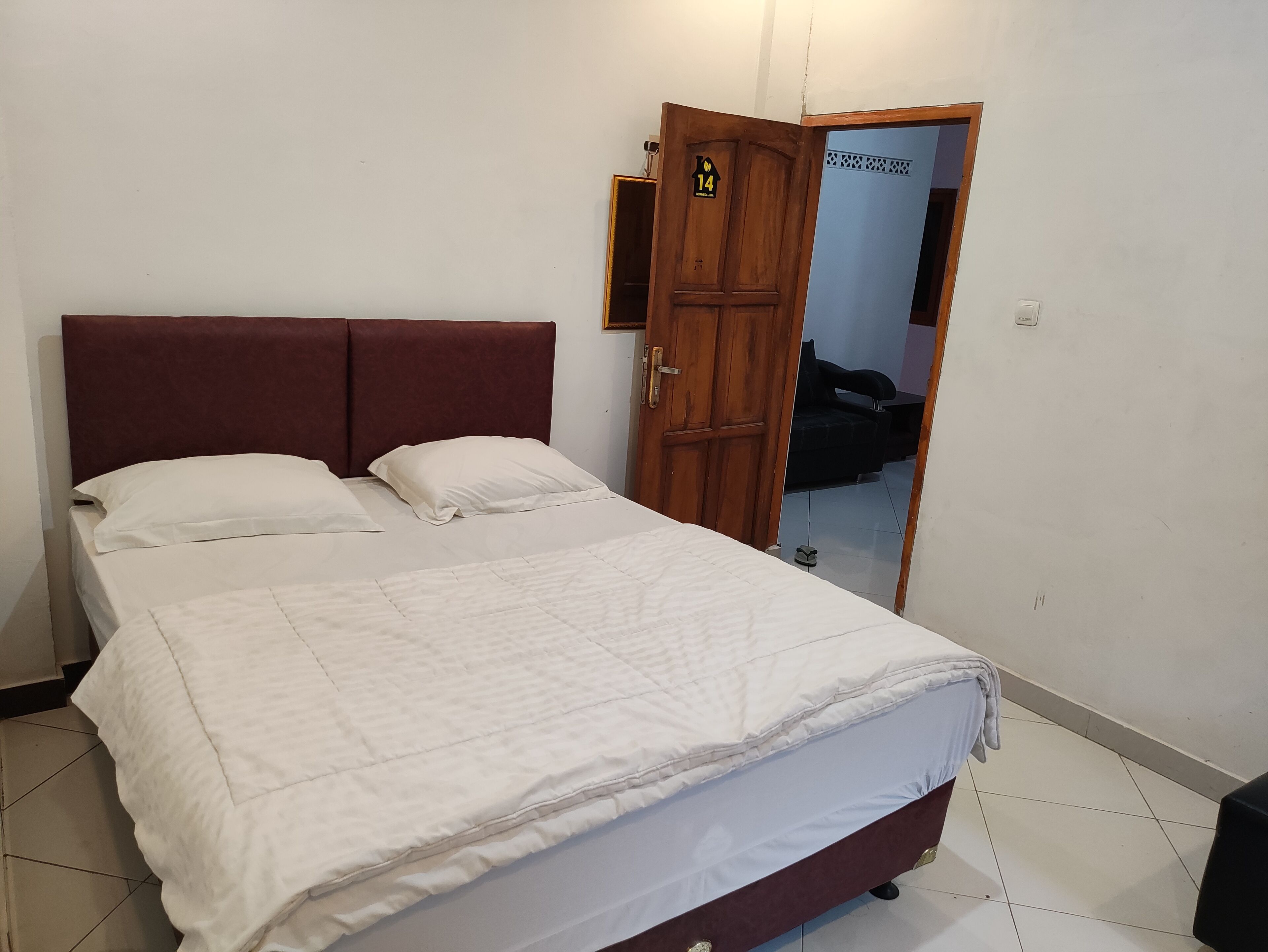 Una cama bien hecha con edredón blanco y almohadas, un cabecero de madera y una puerta con el símbolo del número.