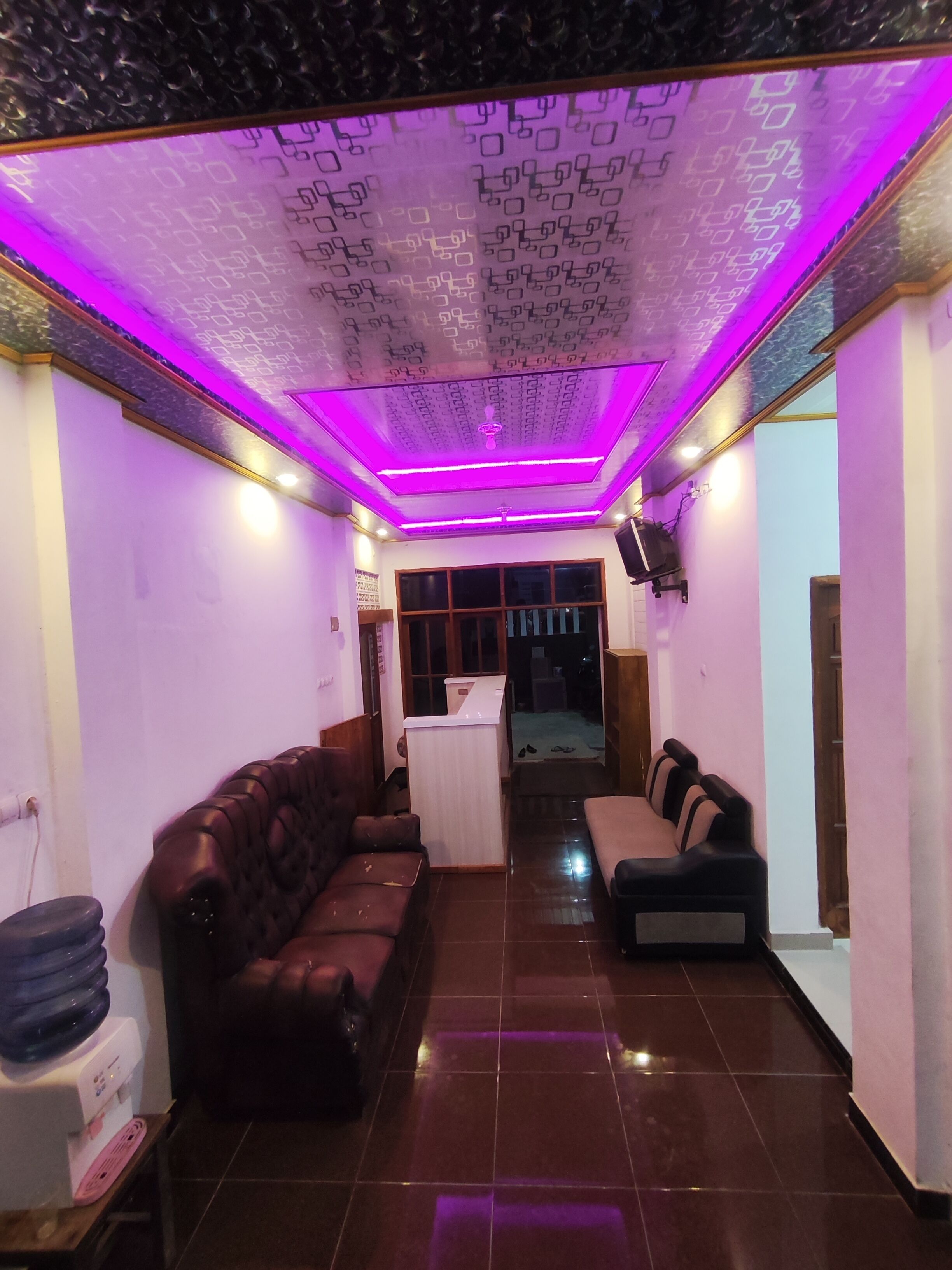 A room with a patterned ceiling, a brown leather sofa, a white table, and a black sofa.