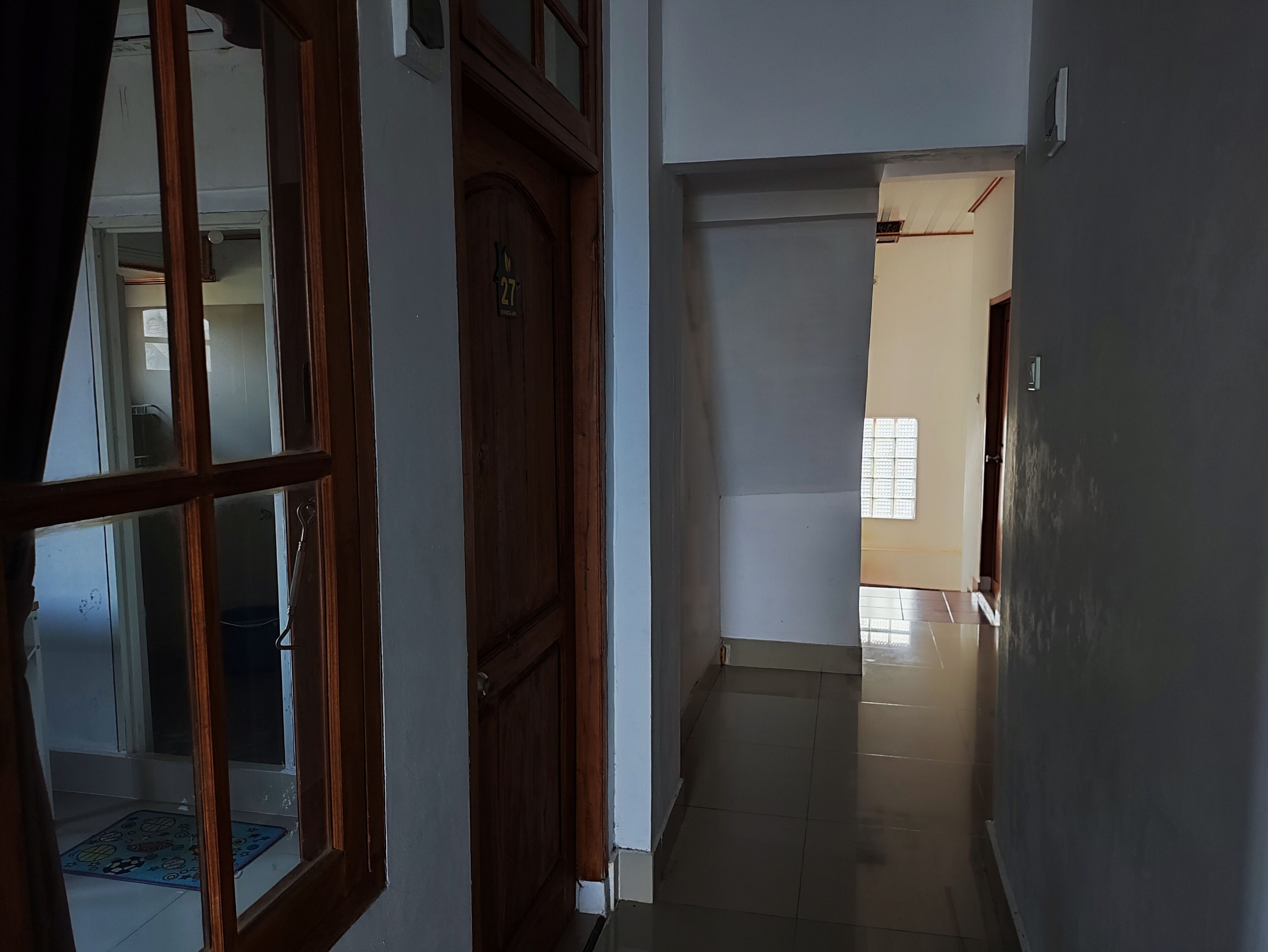 A hallway with a wooden door marked with the number 27, leading to a room with a window.