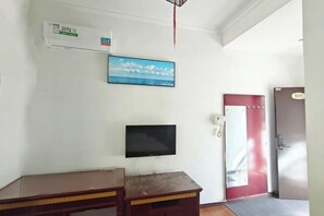 A hotel room with a flat-screen TV mounted on the wall, a wooden desk, a red door, and a wall-mounted air conditioning unit. - Yunjin Hotel (Yangbi)