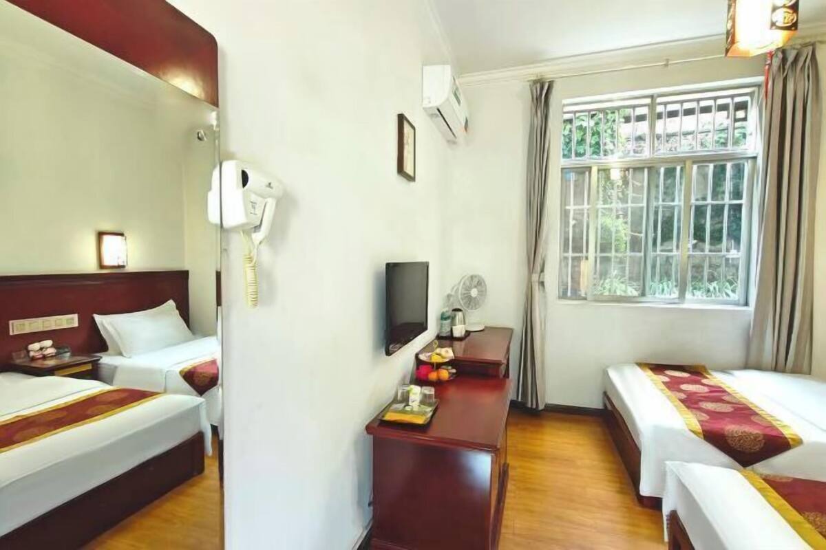 A hotel room with two beds, a desk, a chair, a TV, an air conditioner, and a window with curtains.