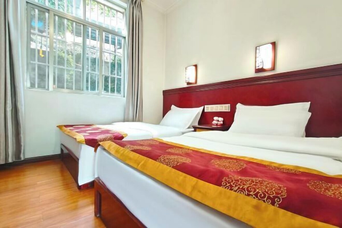 A hotel room with two beds, a large window, and a red headboard.