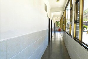 A corridor with a tiled floor, large windows, and doors leading to rooms.