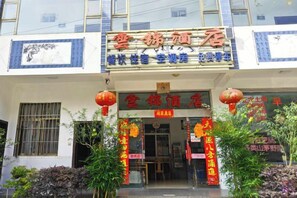 L’entrée d’un hôtel, avec un panneau indicateur, une porte et quelques plantes.
