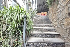Un escalier en pierre menant à un bâtiment, avec une rambarde métallique sur la gauche et un mur sur la droite.