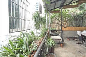 An outdoor patio with a table and chairs, surrounded by potted plants and a view of a building.