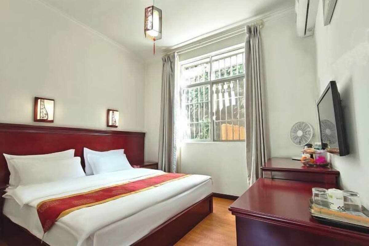 A hotel room with a bed, a desk, a fan, and a window with curtains.