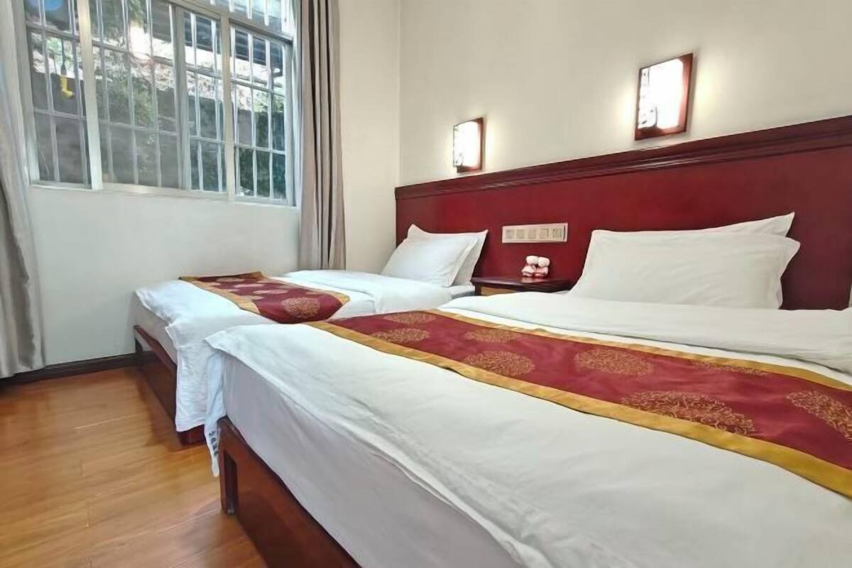 A hotel room with two beds, a wooden headboard, a window, and a nightstand with a lamp.