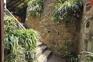 A stone wall with steps leading up to a covered area, surrounded by various plants. - Yunjin Hotel (Yangbi)