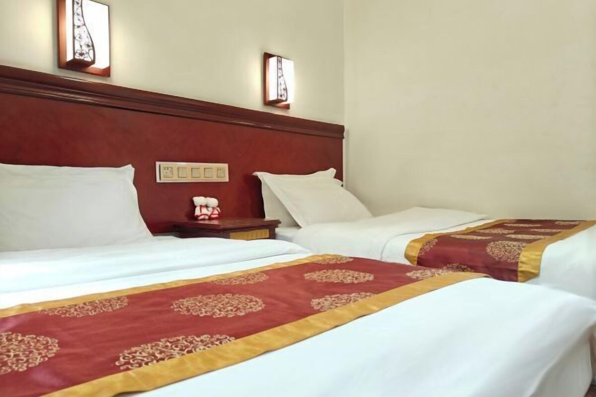 A hotel room with two beds, a wooden headboard, bedside tables, and wall-mounted light fixtures.