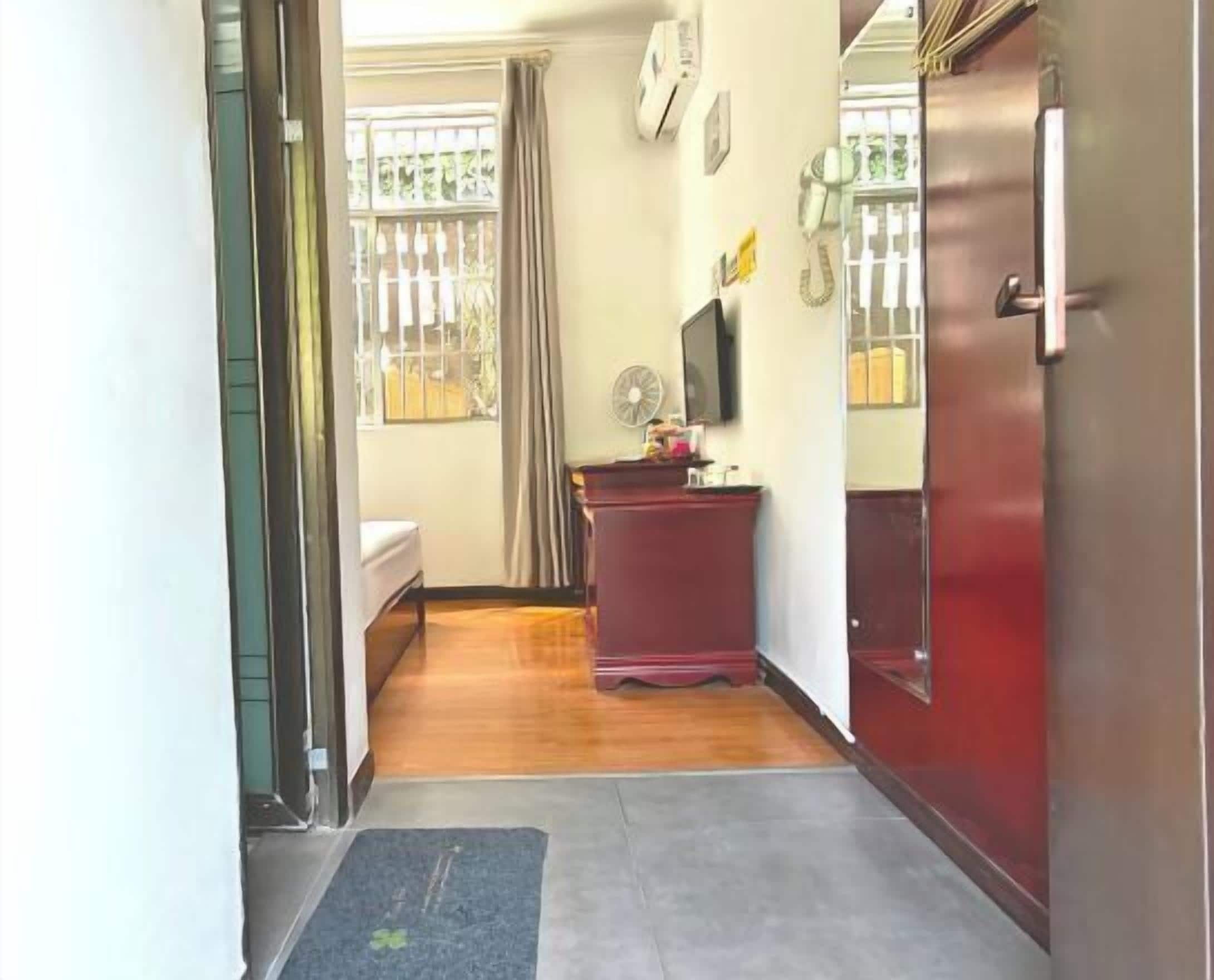 A hallway with a bed, a desk, a fan, and a door.