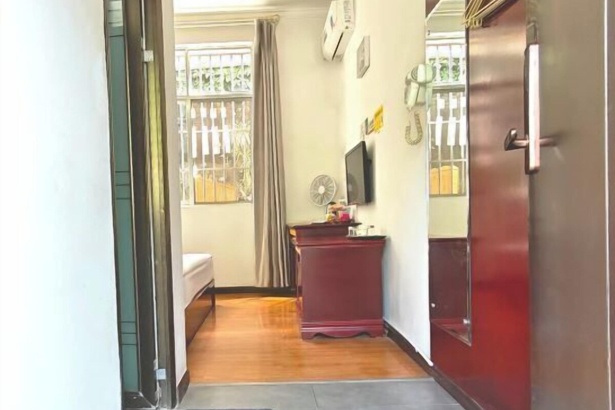 A hallway with a bed, a desk, a fan, and a door.
