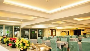 A dining area with tables and chairs, a long counter with floral centerpieces, and a modern ceiling design. - Longhua Hotel (West Ring Road (Karamay)
