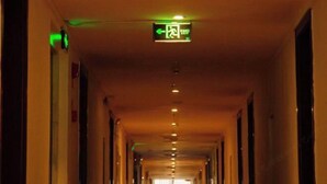 A hallway with a green exit sign and a ceiling light fixture. - Longhua Hotel (West Ring Road (Karamay)