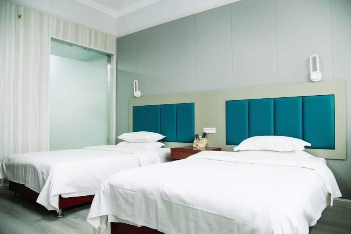 A hotel room with two single beds, a large mirror, and a nightstand with a phone and a lamp.