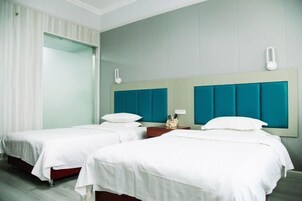 Habitación de hotel con dos camas individuales, un espejo grande y una mesita de noche con teléfono y lámpara.