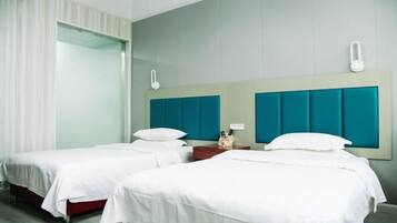 A hotel room with two beds, a large window with curtains, and a teal-colored headboard.