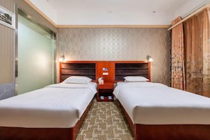 Habitación de hotel con dos camas individuales, cabecero de madera, alfombra estampada y una pared con diseños circulares.