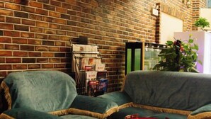 A cozy living area with a brick wall, two green sofas, a red coffee table, and a bookshelf with magazines. - Longhua Hotel (West Ring Road (Karamay)