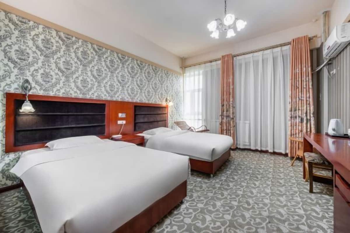 A hotel room with two beds, a wooden headboard, a patterned carpet, a desk, and a window with curtains.
