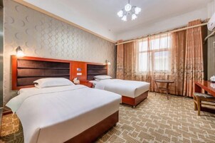 Habitación de hotel con dos camas, un escritorio, una silla, una mesita y una ventana con cortinas.