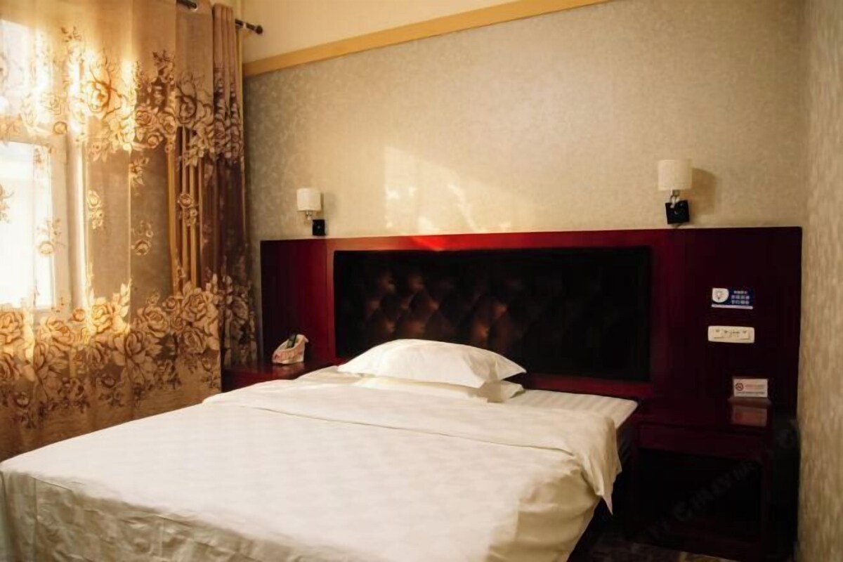 Hotellihuone, jossa on suuri sänky, pääty, kaksi yöpöytävalaisinta ja yöpöytä, jossa on puhelin.
